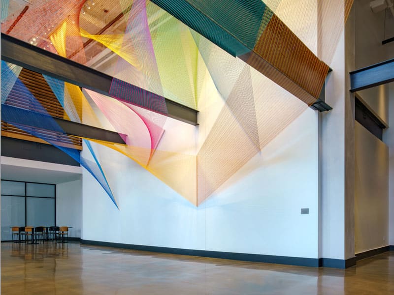 Modern lobby art installation featuring abstract lines and circular forms near building elevators