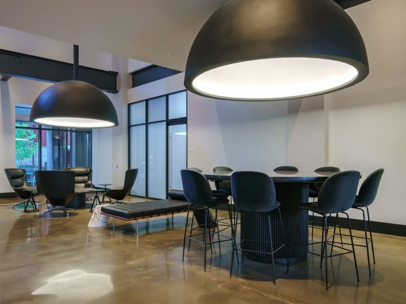 Lounge area in a modern building, featuring dark chairs, round tables, and oversized lighting